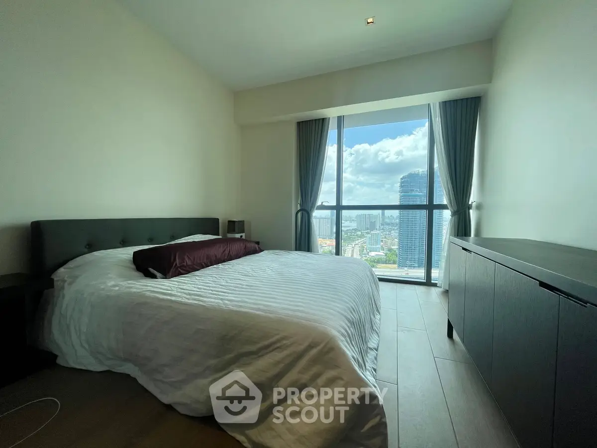 Spacious bedroom with city view and modern furnishings in high-rise apartment.