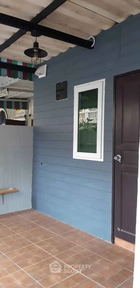 Charming exterior with blue siding and tiled floor, featuring a modern light fixture and window.