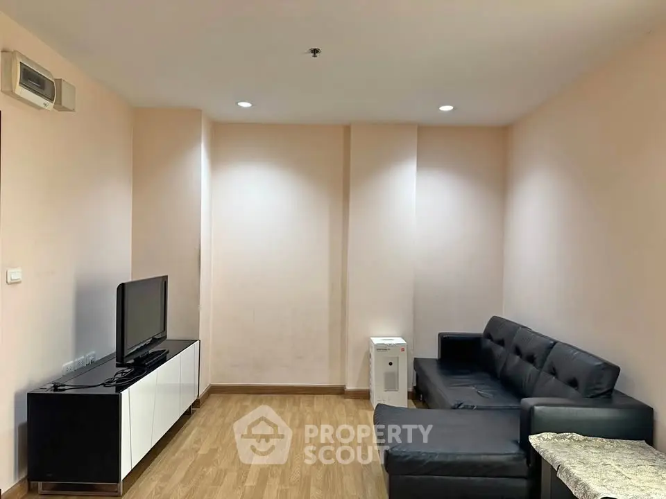 Modern living room with sleek black sofa and flat-screen TV on wooden flooring.