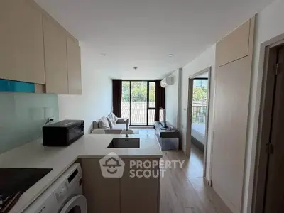 Modern apartment interior with open kitchen and cozy living room, featuring large windows and natural light.