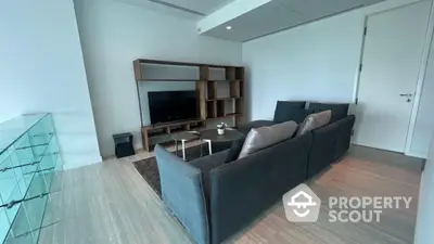 Spacious modern living room with elegant grey sofa, sleek wooden flooring, and a sophisticated entertainment unit, perfect for urban living.