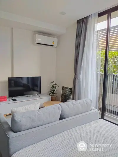 Cozy and modern living room with plush sofa, flat-screen TV, and abundant natural light streaming in from the sliding glass door leading to a refreshing balcony.