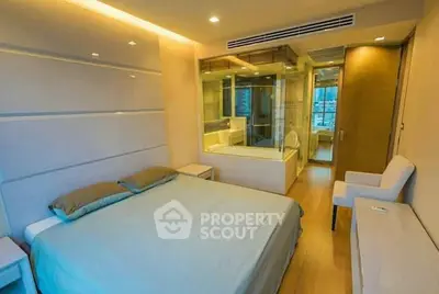 Modern bedroom with ensuite bathroom featuring glass partition and elegant lighting.