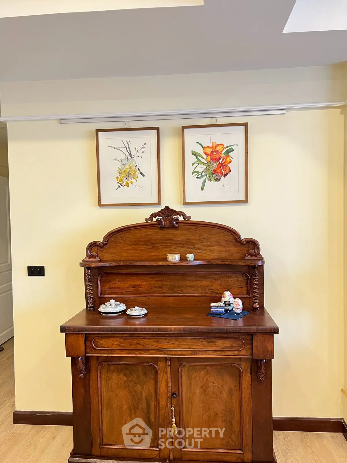 Charming interior with vintage wooden cabinet and floral artwork on cream walls.