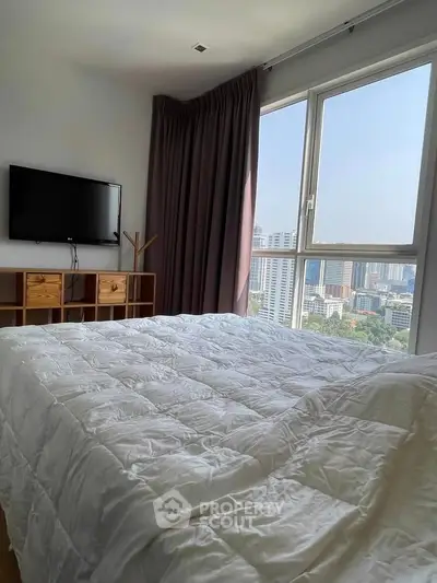 Spacious bedroom with city view, featuring a cozy bed and wall-mounted TV, perfect for urban living.