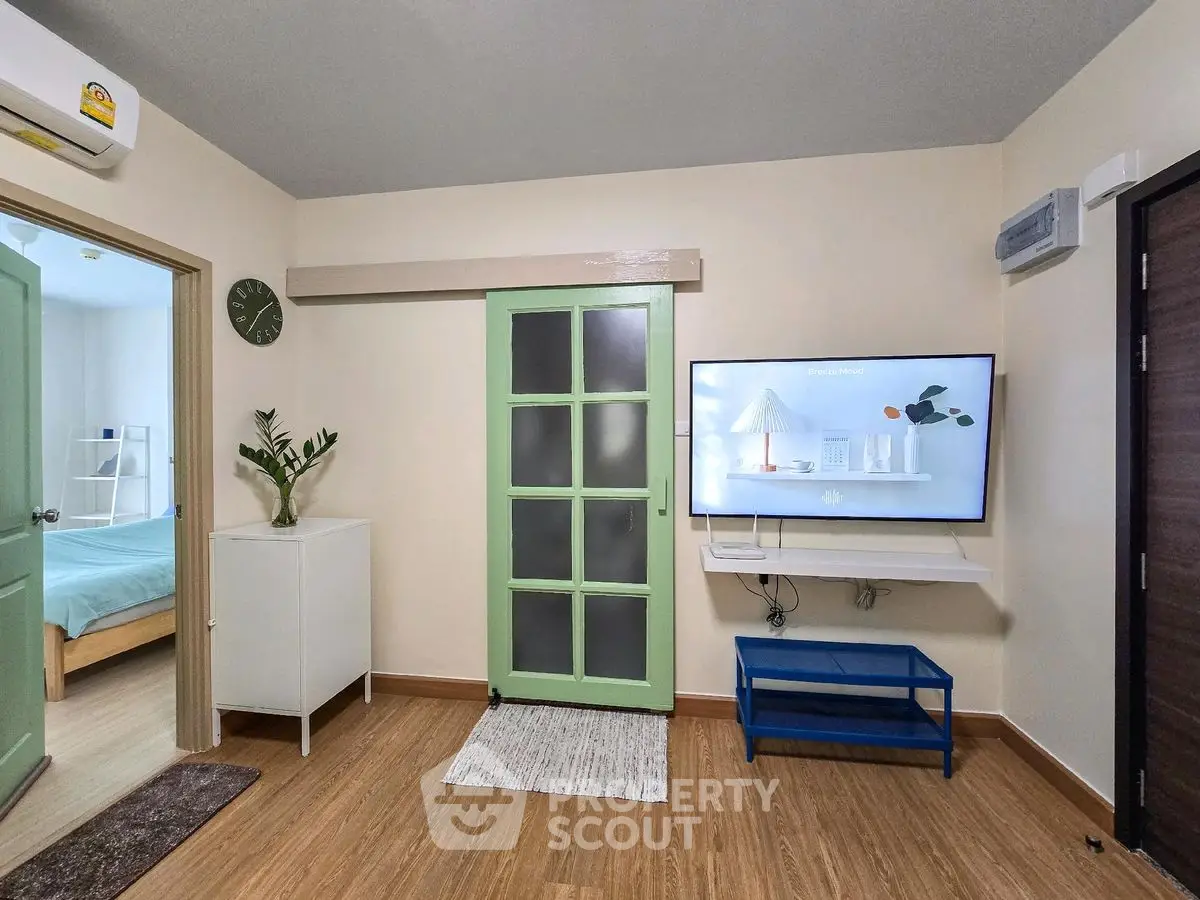 Charming living room with modern decor and wall-mounted TV, featuring a green door and stylish flooring.