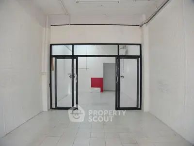 Spacious white-tiled room with glass doors, ideal for commercial use.