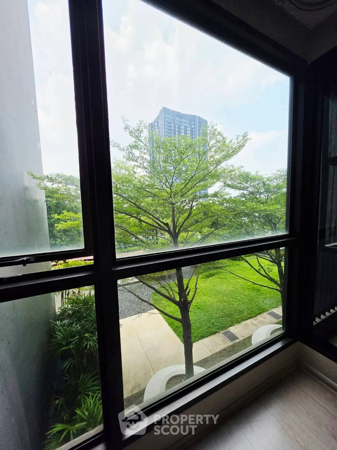 Stunning view from a modern apartment window overlooking lush greenery and a distant high-rise building.