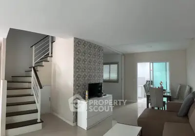 Modern living room with staircase and dining area, featuring sleek design and neutral tones.
