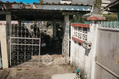 Charming rustic entrance with ornate gate and covered parking area in a cozy residential setting.