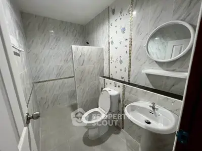 Modern bathroom with elegant tile design and round mirror, featuring a toilet and sink.