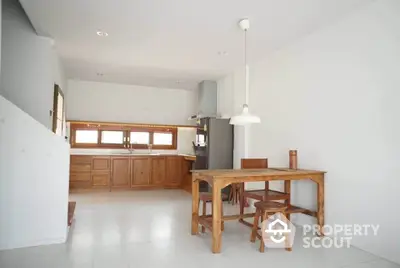 Minimalist kitchen with wooden dining table and stools, featuring a closed layout and ample natural light.