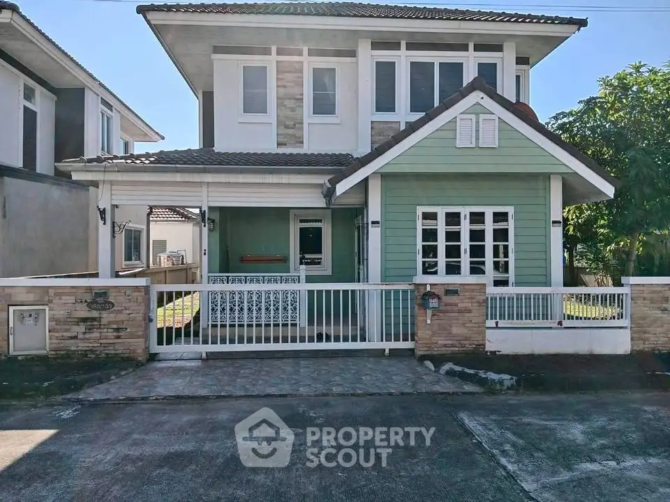 Charming two-story house with green facade and white accents, featuring a gated front yard in a serene neighborhood.