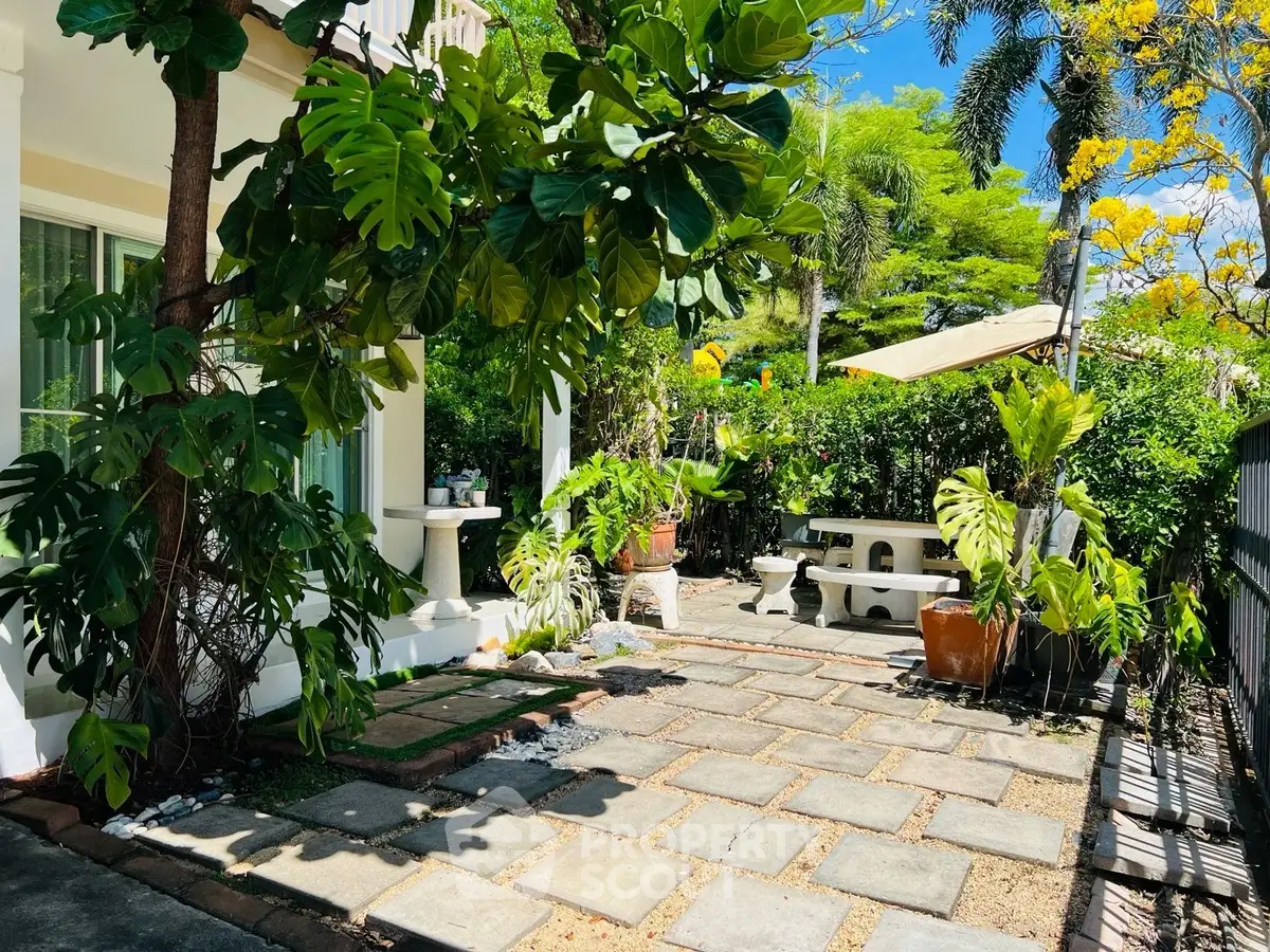 Charming garden patio with lush greenery and stone pathway, perfect for outdoor relaxation.