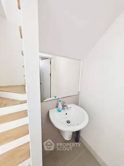 Compact bathroom with white sink and mirror under staircase