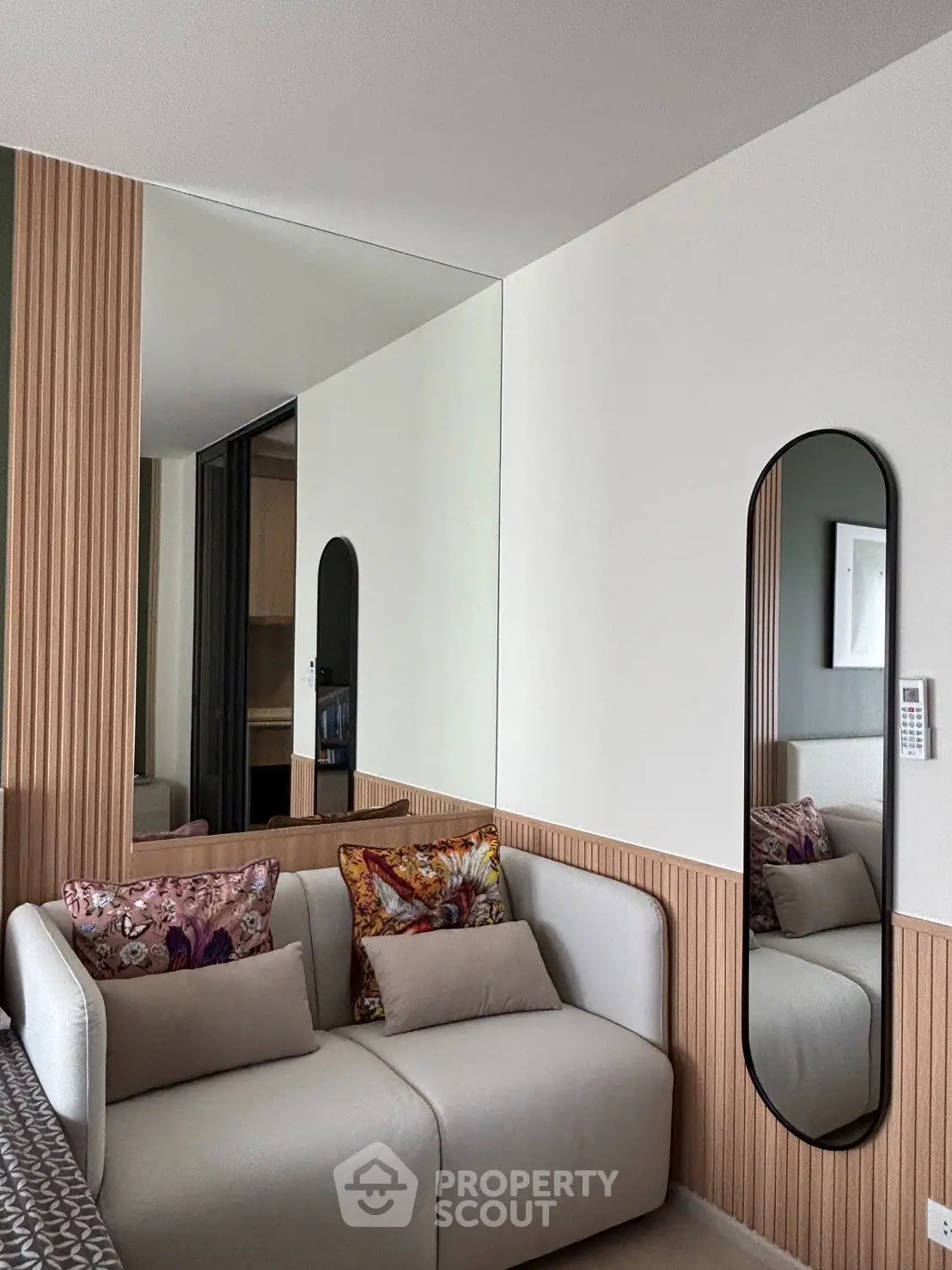 Modern living room with stylish sofa and decorative pillows, featuring a sleek wall mirror and wood panel accents.