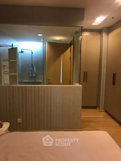Modern bedroom with glass-walled ensuite bathroom and sleek storage solutions.