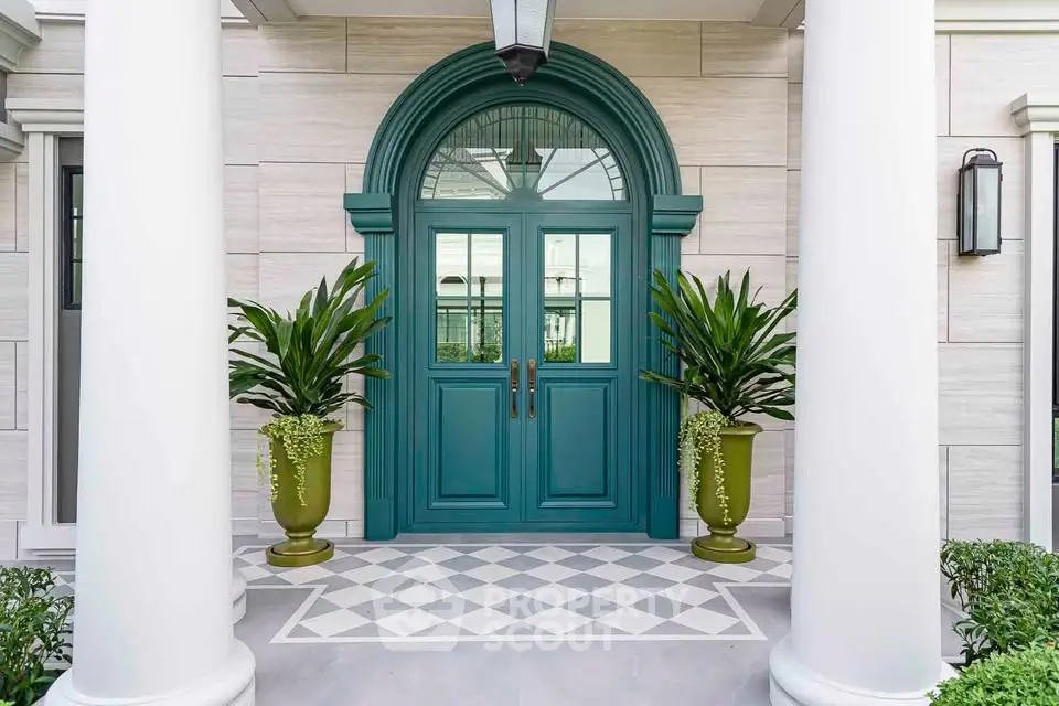Elegant entrance with teal double doors and classic columns, flanked by lush potted plants.