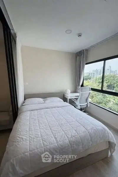 Modern bedroom with large windows offering a stunning city view, featuring a cozy bed and a sleek study desk.