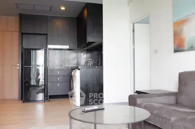 Modern apartment interior with sleek kitchen and cozy living area, featuring dark cabinetry and stylish decor.