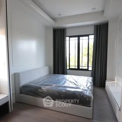Modern bedroom with large window and stylish decor, featuring a comfortable bed and elegant curtains.