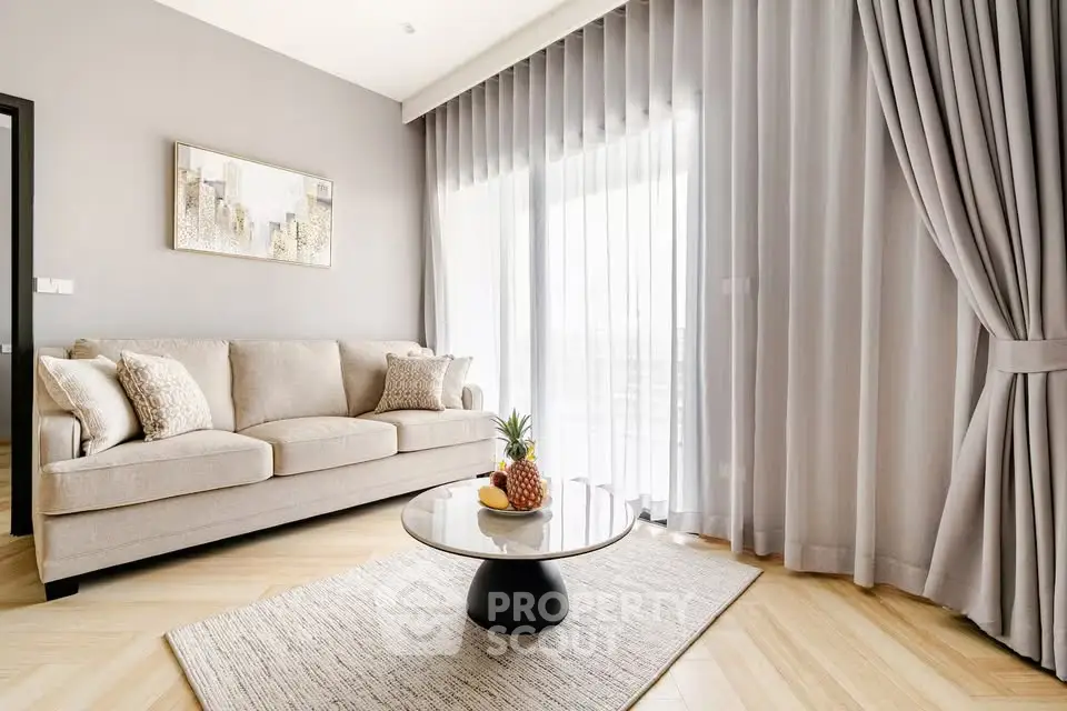 Elegant living room with modern sofa, stylish decor, and large window draped with sheer curtains.