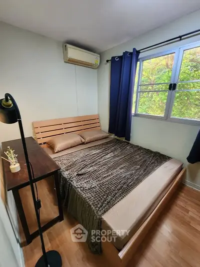 Cozy bedroom with wooden flooring, large window, and air conditioning unit, perfect for relaxation.