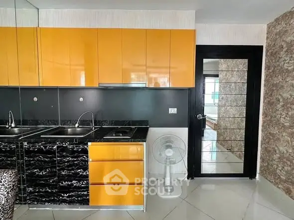 Modern kitchen with vibrant orange cabinets and sleek black countertops.