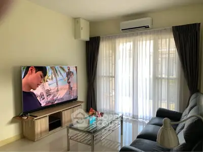 Modern living room with large TV, sleek furniture, and natural light from big windows.