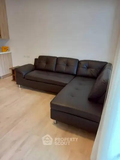 Modern living room with sleek black leather sectional sofa and light wood flooring.