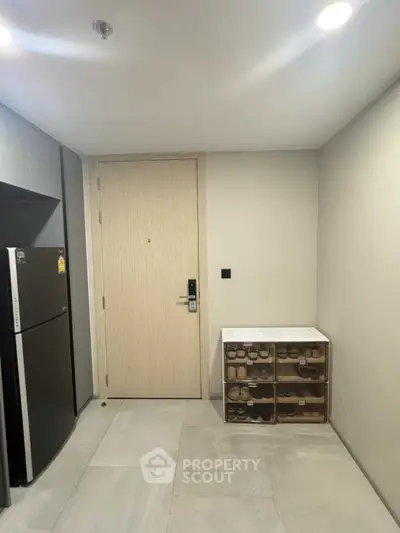 Modern apartment entryway with shoe storage and sleek refrigerator.
