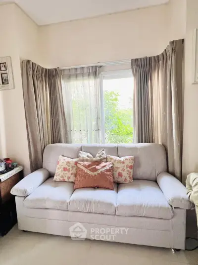 Cozy living room with elegant sofa and floral cushions, bright natural light through large window.