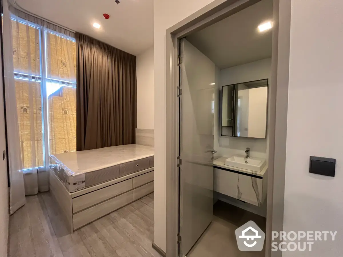 Cozy bedroom with attached modern bathroom, featuring elegant wooden flooring and ample natural light, perfect for restful living.