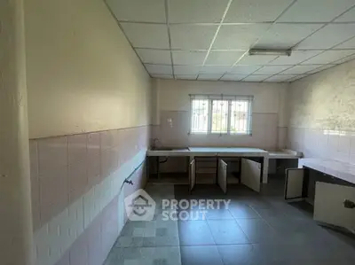 Spacious kitchen with tiled flooring and ample natural light, featuring open cabinets and a large window.