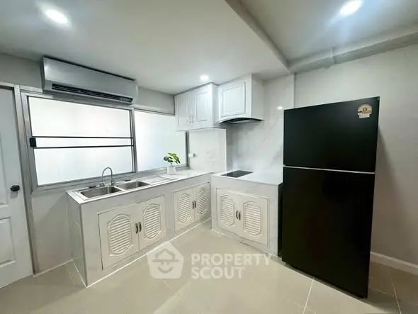 Modern kitchen with sleek black fridge and white cabinetry, featuring a minimalist design and ample storage space.