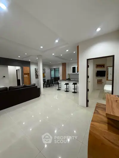 Spacious open-plan living room with modern kitchen and dining area, featuring sleek design and ample lighting.