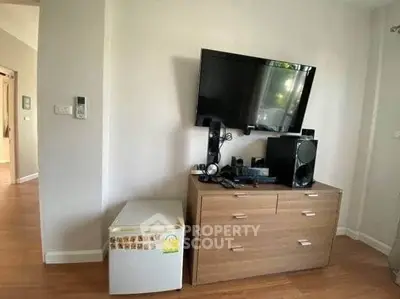 Modern living room with TV, sound system, and mini fridge on wooden cabinet.
