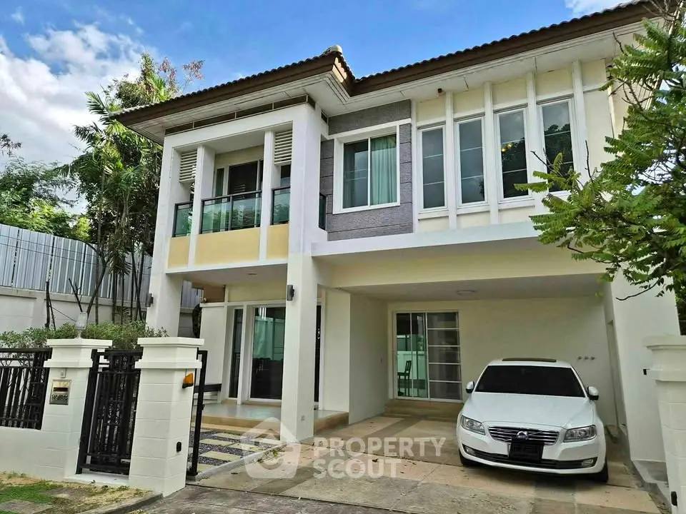 Modern two-story house with carport and lush greenery in a serene neighborhood.