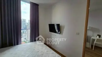Modern bedroom with city view, featuring a wall-mounted TV and large window with curtains.