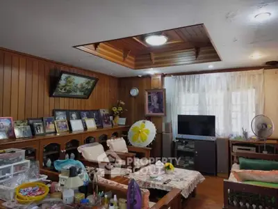 Charming living room with wooden paneling and cozy seating, featuring a TV and decorative elements.