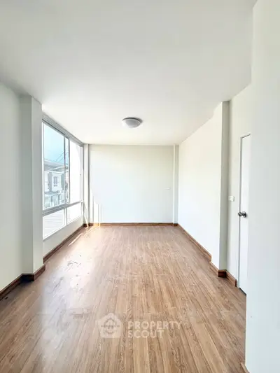 Spacious empty room with large windows and wooden flooring, perfect for customization.