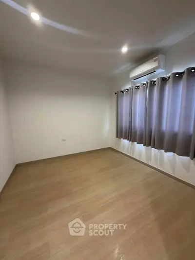 Spacious empty room with wooden flooring and air conditioning, perfect for customization.
