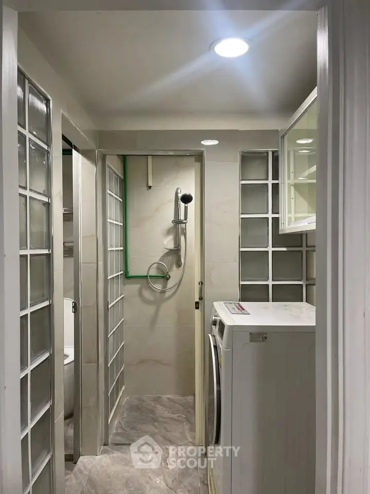Compact bathroom with washing machine and shower, featuring modern glass block design.