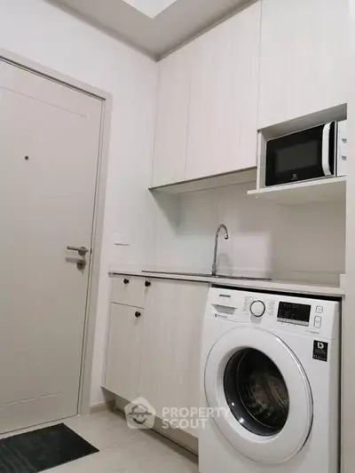 Modern compact kitchen with washing machine and microwave in sleek white cabinetry.