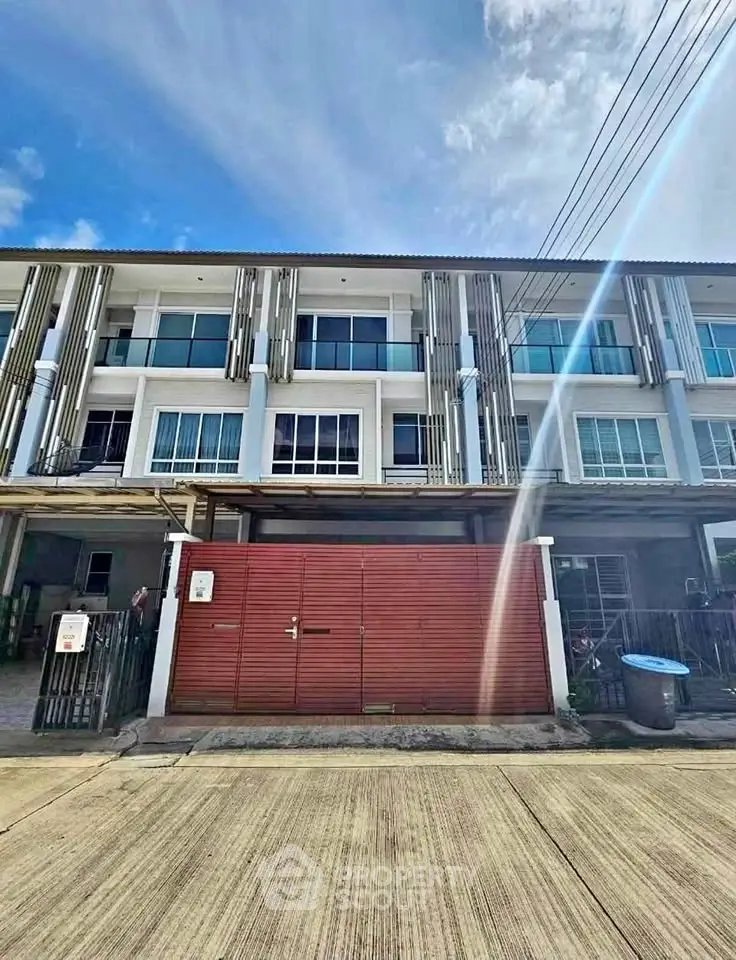 Modern three-story townhouse with stylish facade and gated entrance under a clear blue sky.