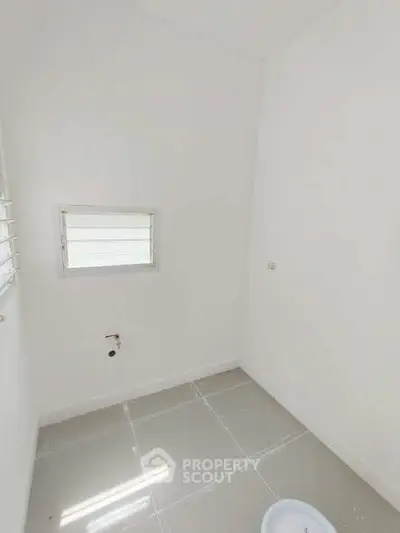 Bright and minimalistic small room with tiled floor and a window, ideal for storage or utility use.