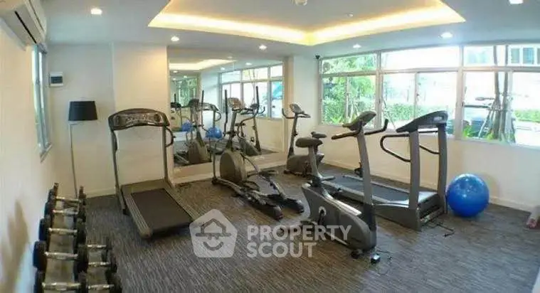 Modern gym with cardio equipment and weights in a bright, spacious room with large windows.