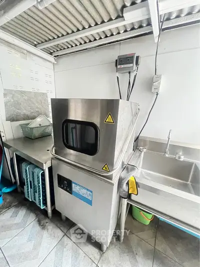 Commercial kitchen with industrial dishwasher and stainless steel sink
