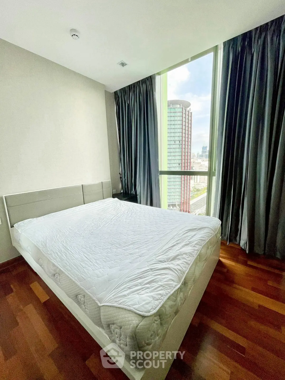 Modern bedroom with large window offering city view and wooden flooring.