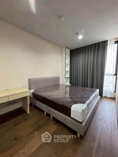 Modern bedroom with stylish bed and floor-to-ceiling window offering natural light and city view.